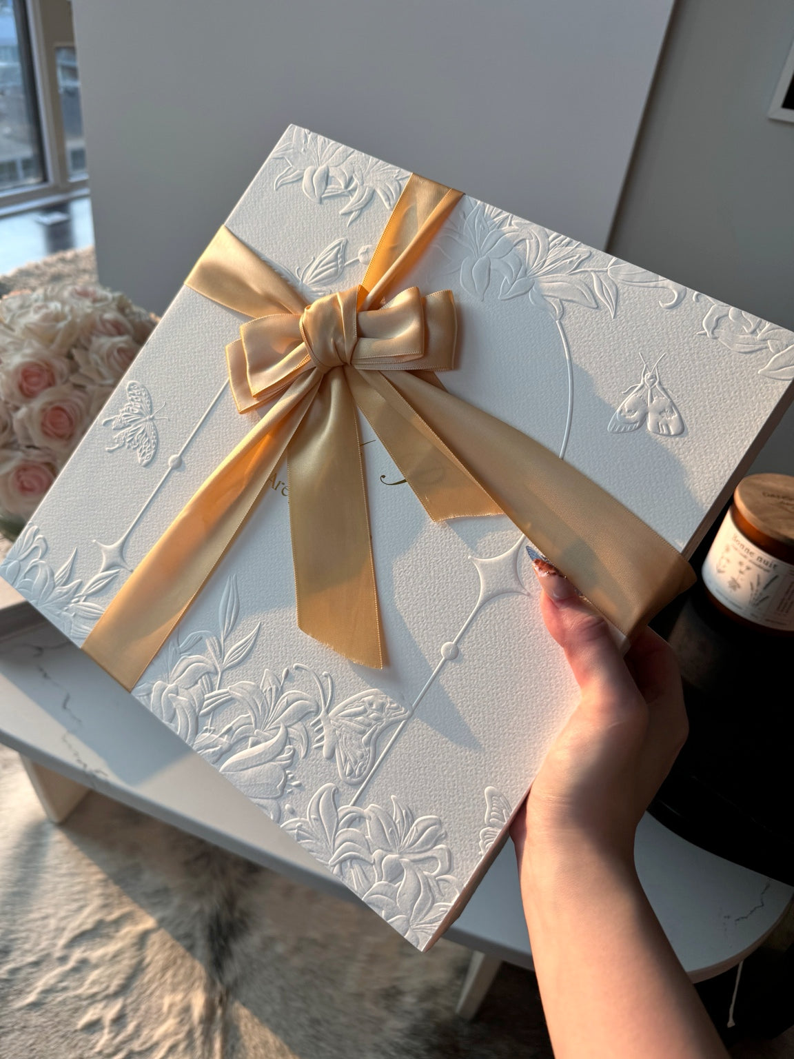 Posoulo white relief-printed gift box with gold ribbon held in natural sunlight